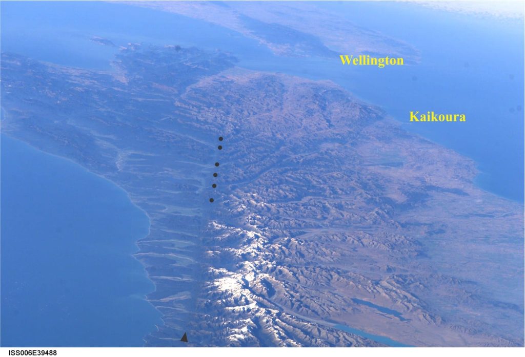 An oblique view of Alpine Fault from the International Space Station. The master fault is a prominent linear feature immediately left of the snow line (black arrow, bottom). The intersection of splay faults that trend northeast indicated by black dots. The fault splays are clearly delineated by valleys. Image Credit: NASA ISS006E39488 