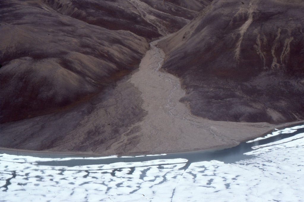A small drain basin that acts as a tributary to a larger fiord. The sink in this case is a fan delta, about a kilometre wide at its shoreline (the white is sea ice). Here, Source, transfer zone, and sink are contained within a small area. However, even here there is some grain size fractionation. The left side of the fan delta (dark colours) is inactive and represents longer duration storage of sand and gravel. The delta is probably less than 10,000 years old.