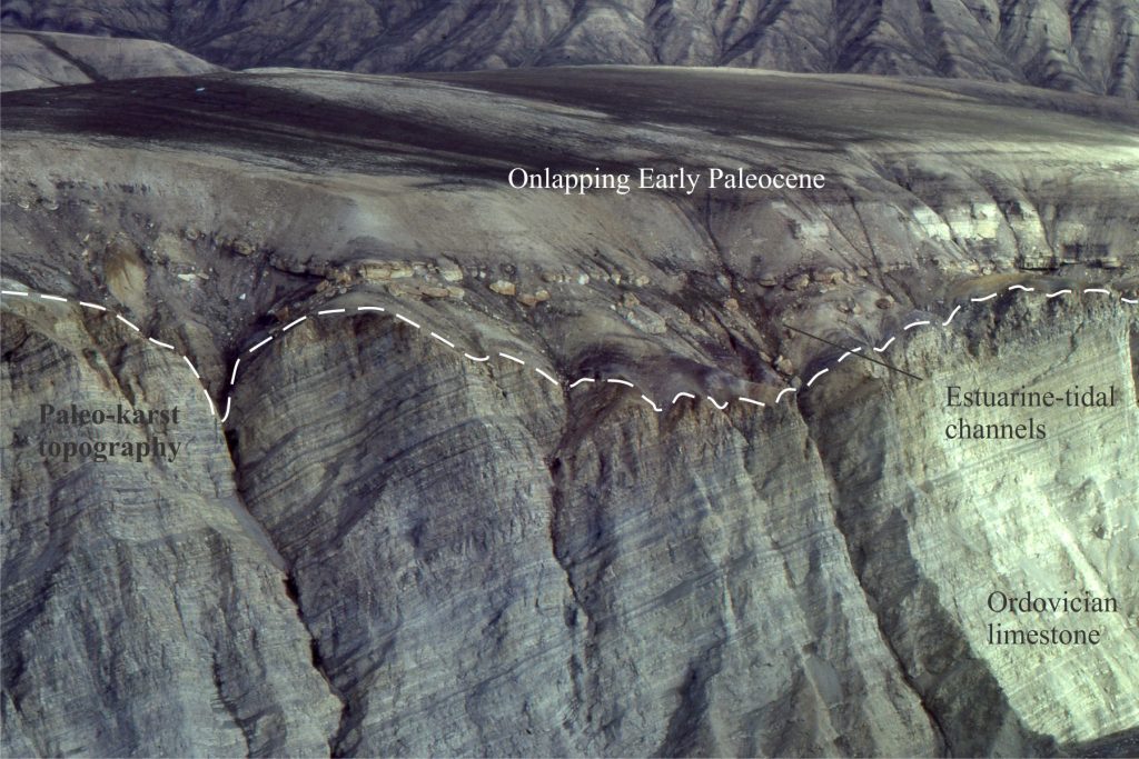 A more expansive view of the Ordovician – Paleocene subaerial unconformity showing the paleotopography developed by karstification during protracted exposure of the Ordovician carbonates (dashed line). The karst surface contains regoliths, dissolution collapse pits, and in places collapse breccias. Lower Paleocene estuarine, tidal channel, sand spit and bar deposits onlap the unconformity from right to left. Same location as above.