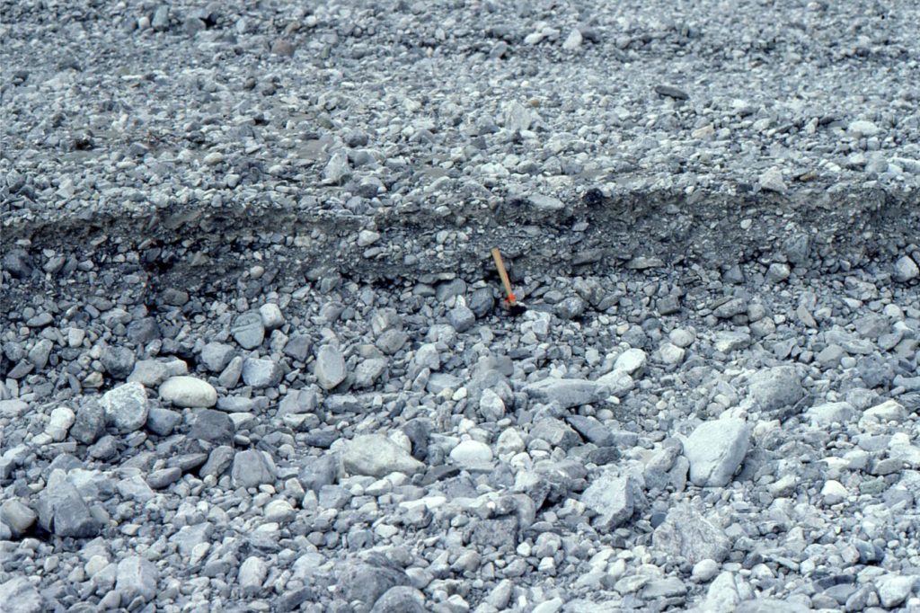Erosional cross-section through a subhorizontal gravel sheet, deposited on an alluvial fan that periodically discharges into Peel River, Yukon. This view shows the crude low angle layering in very poorly sorted gravel. Framework clast sizes range from fine pebble to 150-200 mm diameter cobbles. Matrix is a mix of fine and coarse sand. Flow was left to right. Abandonment of the bar was accompanied by erosion and cannibalization of gravel that was deposited on younger bars farther down the fan slope.