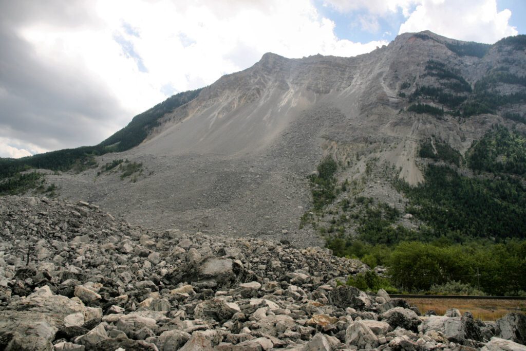 Part of the mountain rock wall and run-out of Frank Slide, a massive, dry rock slope failure that buried part of the Alberta mining town of Frank in 1903. The failure surface can be seen in the limestone ridge behind. Landslide deposits in the foreground are angular and very poorly sorted. Coal mining may have contributed to weakening of fractured rock along the ridge. Image credit: Marek Ślusarczyk 2007, Wikipedia Commons  