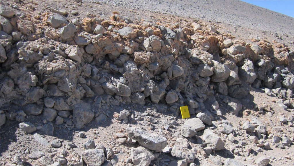 Section through a boulder colluvial deposit on the flanks of an Eocene, andesite volcanic cone. The primary depositional mechanism was rock fall down a talus fan, such that the accumulation is thickest and coarsest at the base of slope (Category 1 in the table above). The angular fragments are close fitting, forming a clast-supported framework with poorly sorted, finer grained clastic material filling the interstices. The top 50-100 cm of the unit are cemented by very porous, ferroan calcite (orange). Chilean Altiplano. The climate here is identical to that in the previous image.
