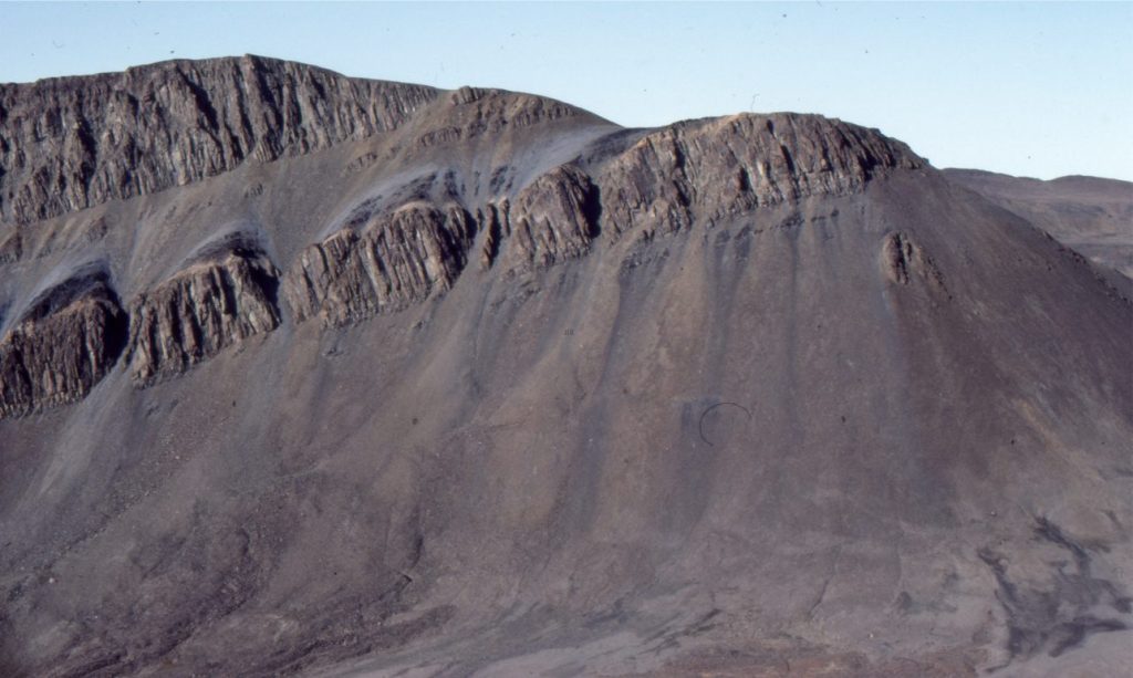 Talus fans exiting joint-controlled erosional notches in diabase sills that intrude Triassic shale, Axel Heiberg Island, Canadian Arctic. The uppermost sill is about 30 m thick. The dominant process here is rock fall (Category 1 in the table above), but slope wash (sheet wash) is also responsible for distributing talus during spring thaw (Category 2), so this colluvium might be categorised as type 3 (hybrid). The talus (colluvium) deposits consist of small shale fragments and larger clasts of diabase; the largest clasts are accumulating at the base of slope.