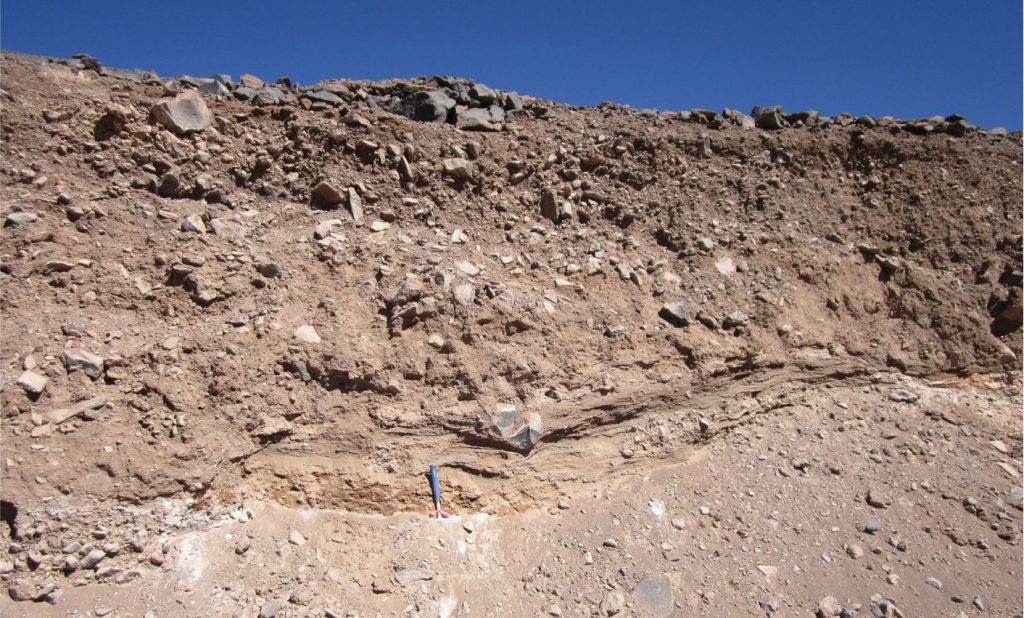 A non-sorted, non-stratified colluvium deposit consisting of angular fragments of andesite derived primarily by seasonal mass wasting of lava flows on the flanks of a Miocene volcano, Chilean Altiplano. The main depositional processes here are rock fall, rolling, downslope sliding, and creep (Category 1 in the table above). The basal layer (at the hammer) contains weak layering possibly derived from slope wash. The climate here is hyper-arid and at elevations greater than 4000 m a.s.l. winter freezing is severe. Most of the mass wasting occurs during spring thaw but sediment transport can also include intermittent sheet floods and debris flows.